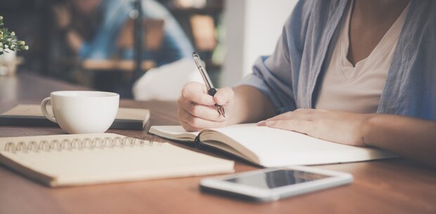 Person sitzt am Schreibtisch und macht sich Notizen.